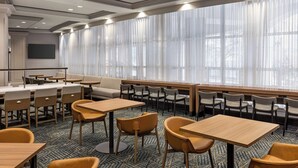A hotel room with a large window, a flat-screen TV mounted on the wall, and a seating area with tables and chairs. - Homewood Suites by Hilton Washington, D.C. Downtown (Washington)