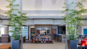 Un vestíbulo amplio con un quiosco central, plantas en macetas grandes y una zona de bar.