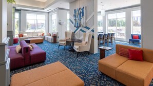Un vestíbulo espacioso con un suelo de alfombra azul estampada, varias zonas de estar que incluyen sofás y sillones, y grandes ventanales con vistas al exterior.