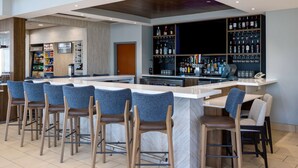 Una zona de bar con varios taburetes, una barra y estantes llenos de botellas y vasos.