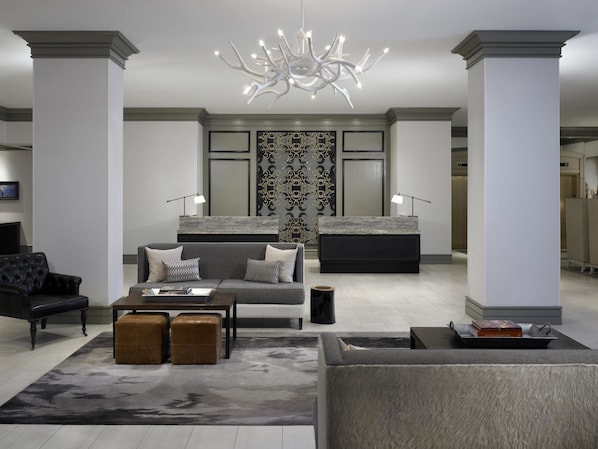 A modern living room with a sofa, ottomans, a coffee table, and a unique chandelier. - Hilton Dallas/Park Cities (Dallas)