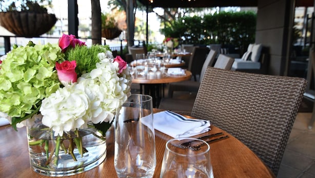 Un espace de restauration en plein air avec des tables disposées pour deux personnes, agrémenté de beaux verres et d’un vase rempli de fleurs.