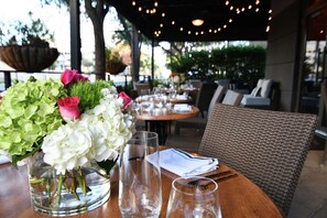 An outdoor dining area with tables set for two, featuring clear glassware and a vase of flowers. - Hilton Dallas/Park Cities (Dallas)