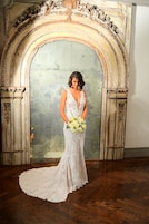 Una novia con un vestido de encaje blanco posa frente a un arco ornamentado y desgastado.