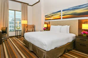 Una habitación de hotel con una cama grande, un escritorio, una silla, una mesita y una ventana con cortinas.
