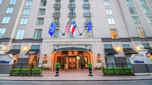 L’entrée d’un hôtel, avec une façade moderne, plusieurs drapeaux et un éclairage soigné.
