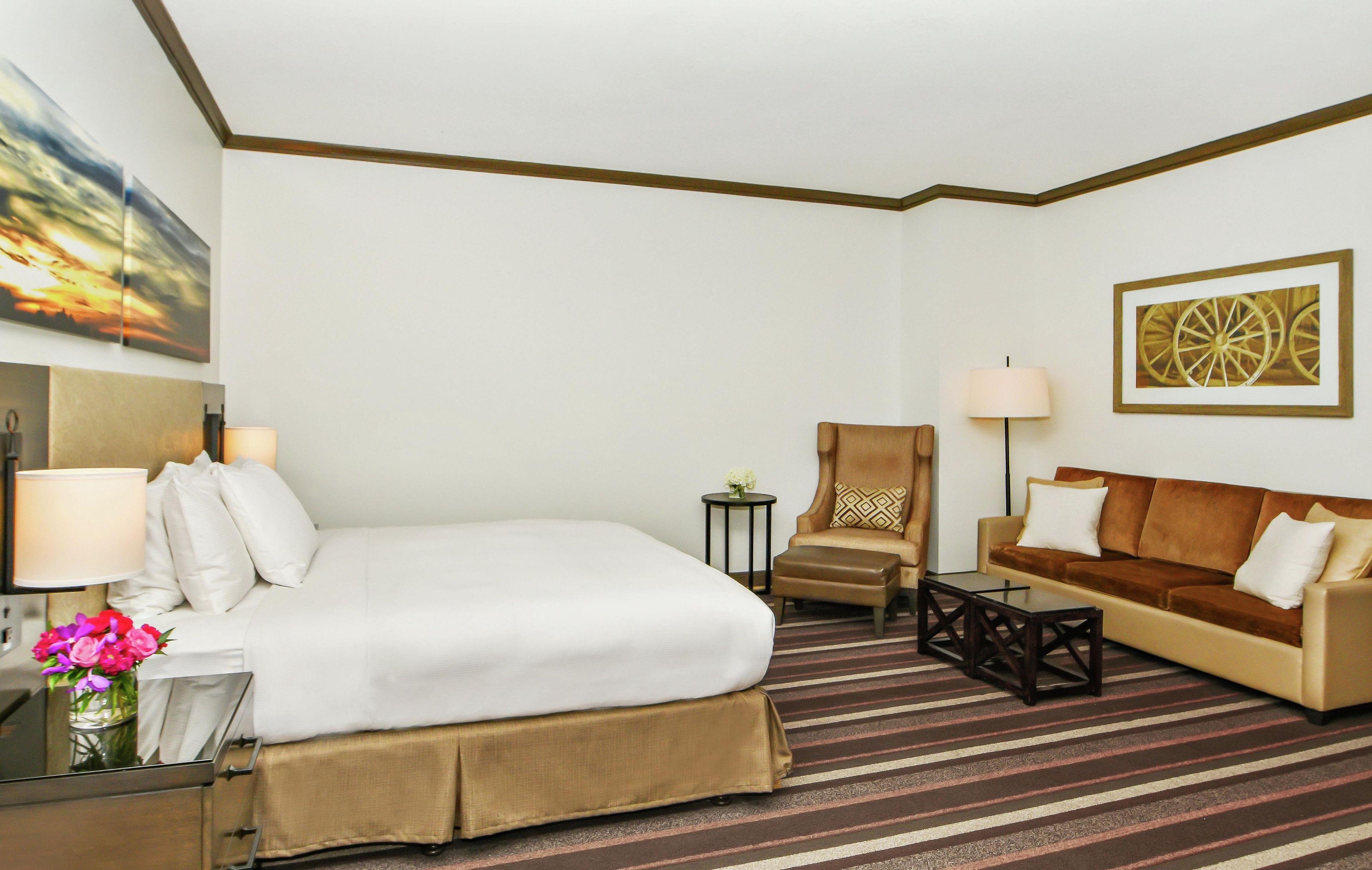 Una habitación de hotel con una cama, un sofá, una silla, una mesita y una lámpara.