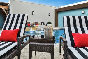 A poolside area with two striped lounge chairs, a small table with bottles, and a view of the pool and building in the background.