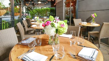 A restaurant with round tables, wicker chairs, and a wooden floor.