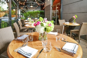 A restaurant with round tables, wicker chairs, and a wooden floor.