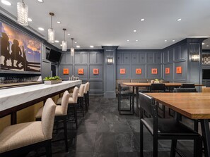 A modern bar area with a marble countertop, bar stools, pendant lighting, and a wall with framed artwork.