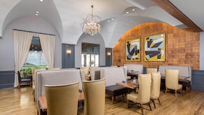 Un restaurant avec de hauts plafonds, un lustre, des banquettes confortables, un plancher en bois et des œuvres d’art abstraites sur les murs.