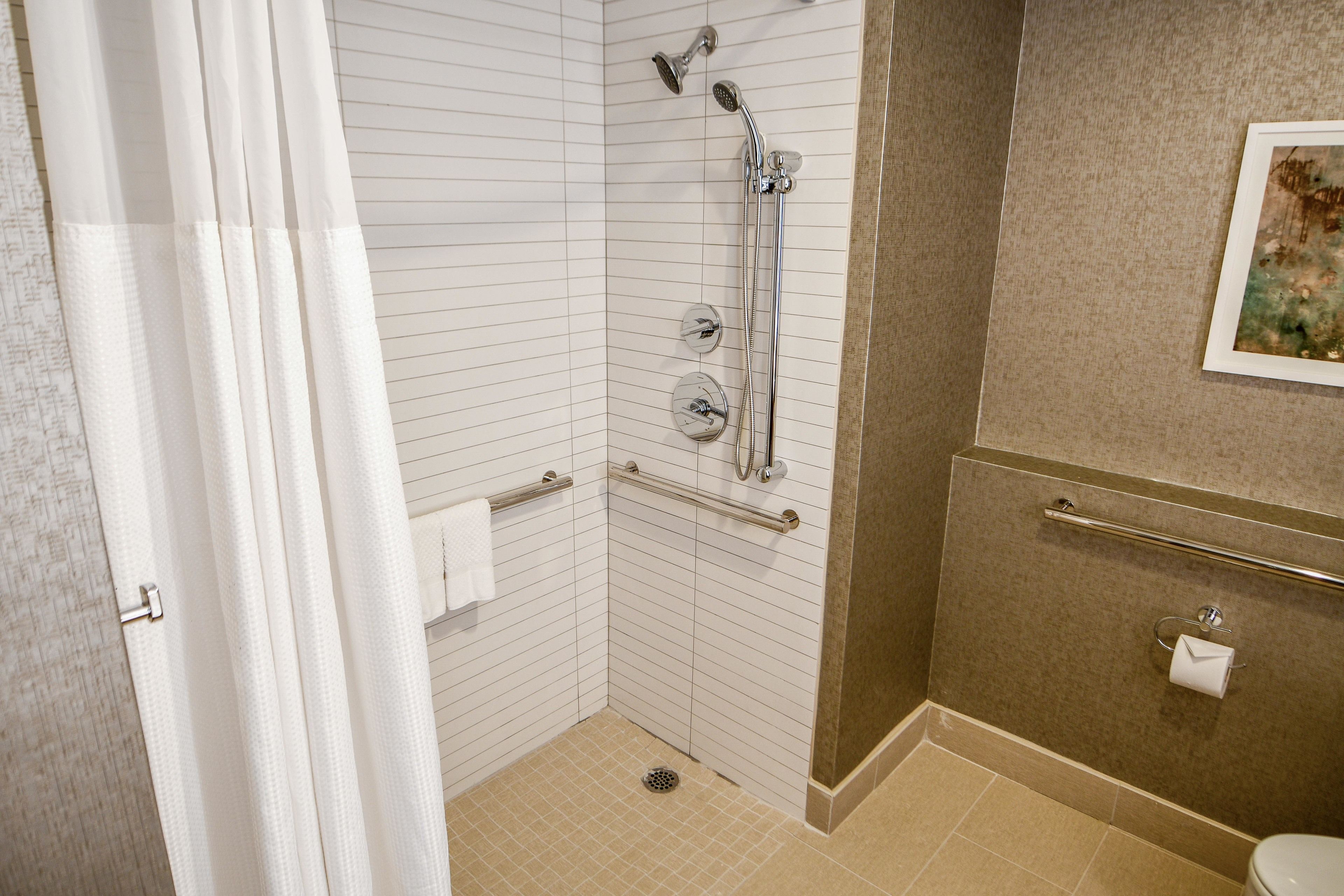 A bathroom with a shower, grab bars, a towel rack, and a toilet paper holder.