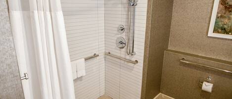 A bathroom with a shower, grab bars, a towel rack, and a toilet paper holder.