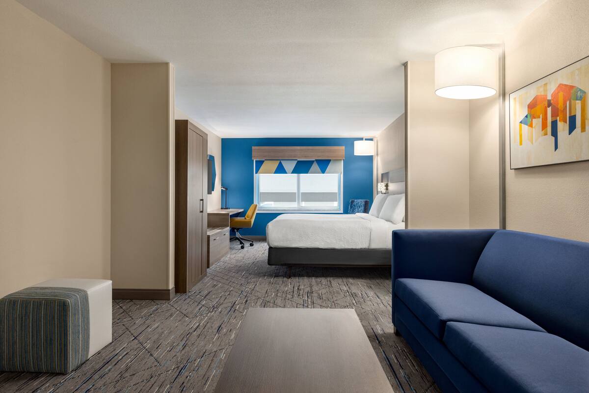 A hotel room with a bed, a blue sofa, a desk, and a chair.