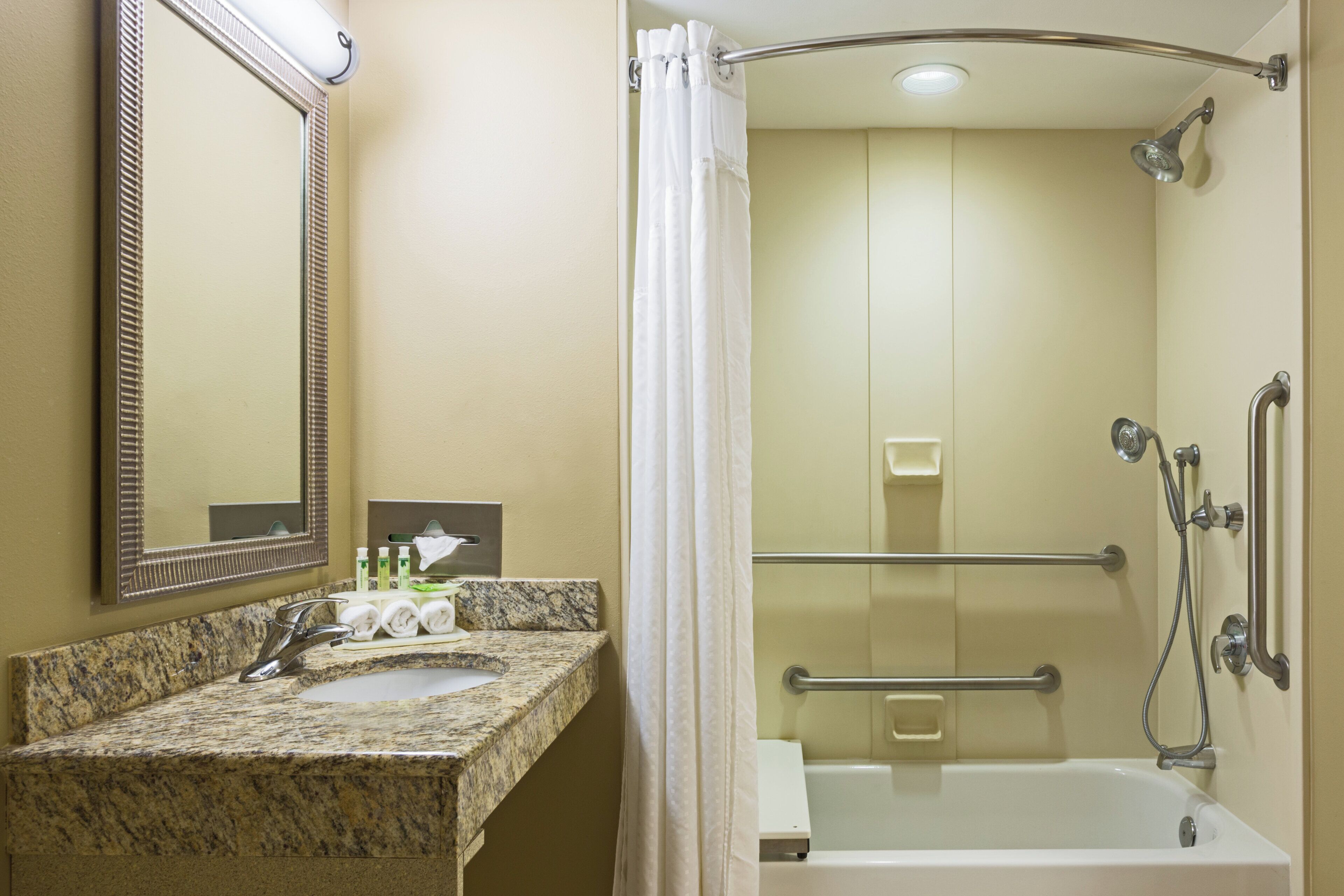 A bathroom with a granite countertop, a sink, a mirror, a shower with a grab bar, and a towel rack.
