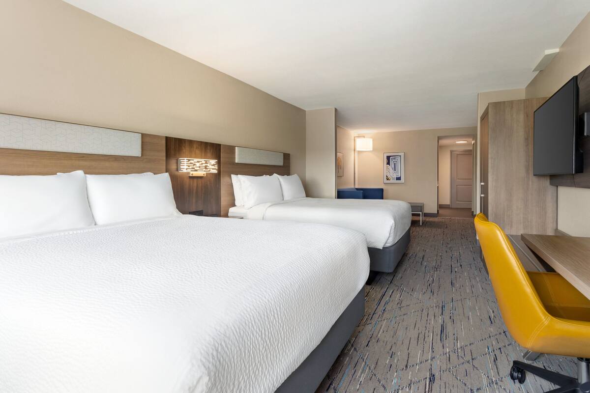 A hotel room with two beds, a desk, a chair, a television, and a carpeted floor.