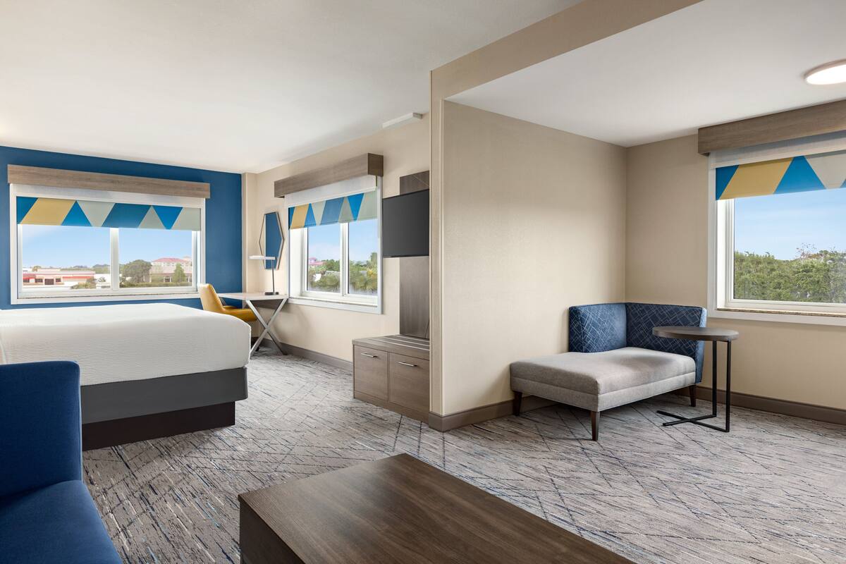 A hotel room with a bed, a desk, a chair, a small table, and a TV.
