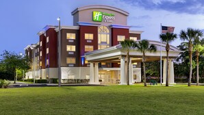 A Holiday Inn Express & Suites building with a well-maintained lawn, palm trees, and an American flag. - Holiday Inn Express Hotel & Suites Fort Pierce West by IHG (Fort Pierce)
