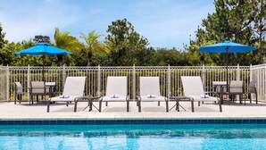 A poolside area with lounge chairs and umbrellas, surrounded by a white fence and trees. - Holiday Inn Express Hotel & Suites Fort Pierce West by IHG (Fort Pierce)