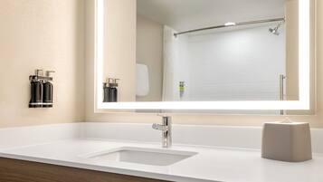 A modern bathroom with a large mirror, a white sink, and a shower area.
