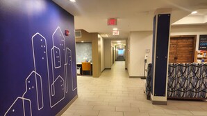 A hotel corridor with a blue wall featuring a geometric pattern, a reception desk, and an exit sign. - Holiday Inn Express Hotel & Suites Idaho Falls by IHG (Idaho Falls)