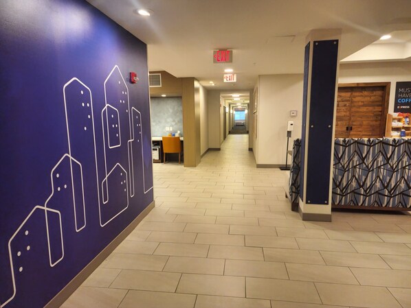Un couloir d’hôtel avec un mur bleu orné d’un motif géométrique, un comptoir d’accueil et un panneau indiquant la sortie.