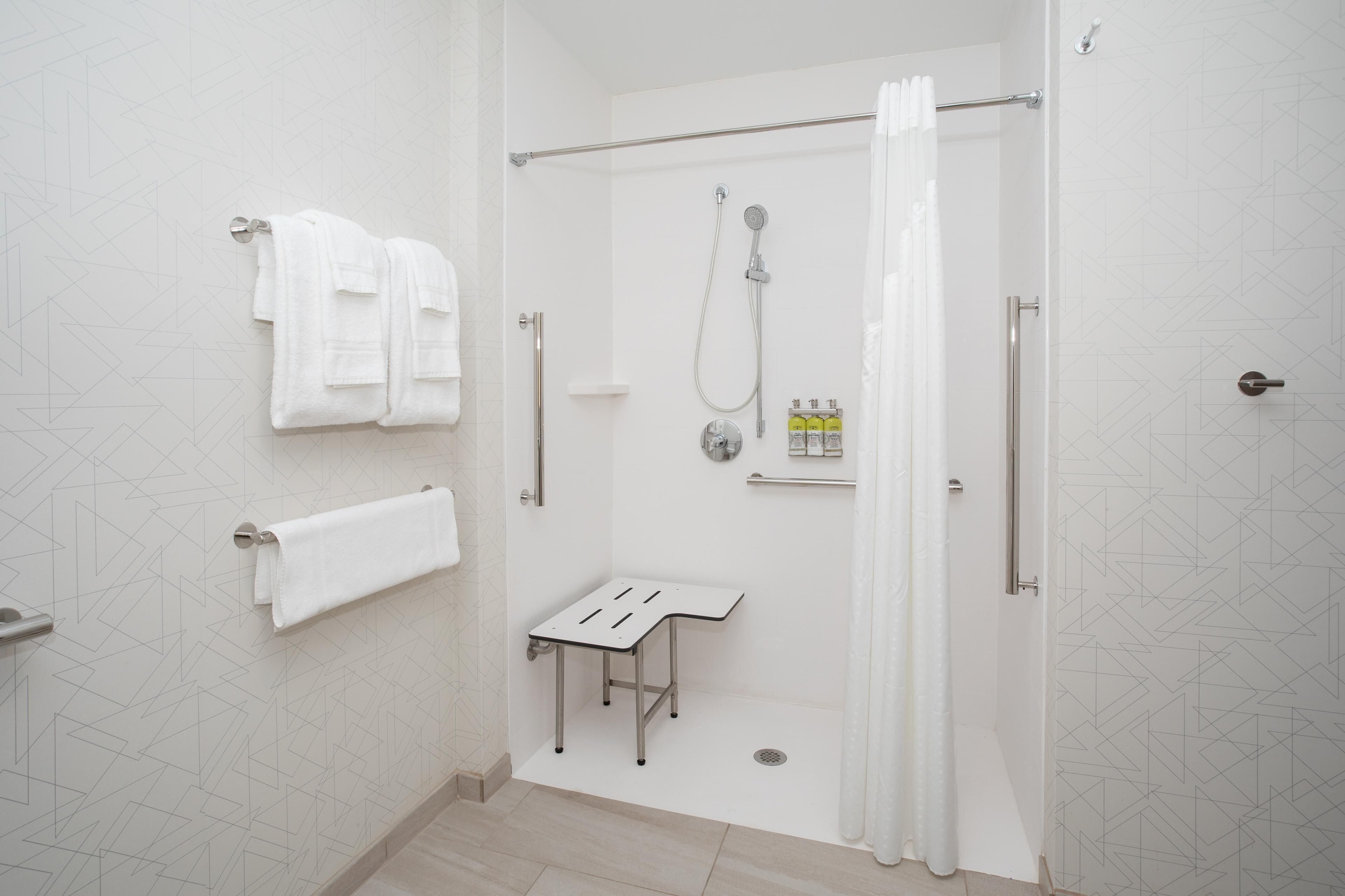 Un baño moderno con puerta de vidrio, un toallero blanco, un cabezal de ducha y una mesita con artículos de aseo.