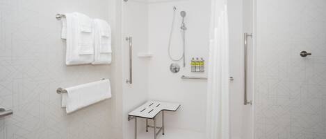Un baño moderno con puerta de vidrio, un toallero blanco, un cabezal de ducha y una mesita con artículos de aseo.