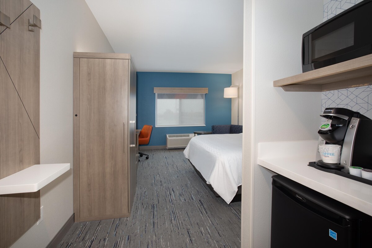 Une chambre d’hôtel comprenant un lit, un bureau avec une machine à café, un four à micro-ondes et une fenêtre avec des stores.