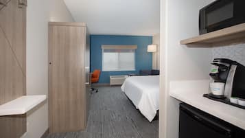 Een hotelkamer met een bed, een bureau met een koffieapparaat, een magnetron en een kledingkast.
