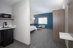 Ein kleines Hotelzimmer mit Küchenzeile, einem Bett, einem Nachttisch, einem Fenster und einem Kleiderschrank.