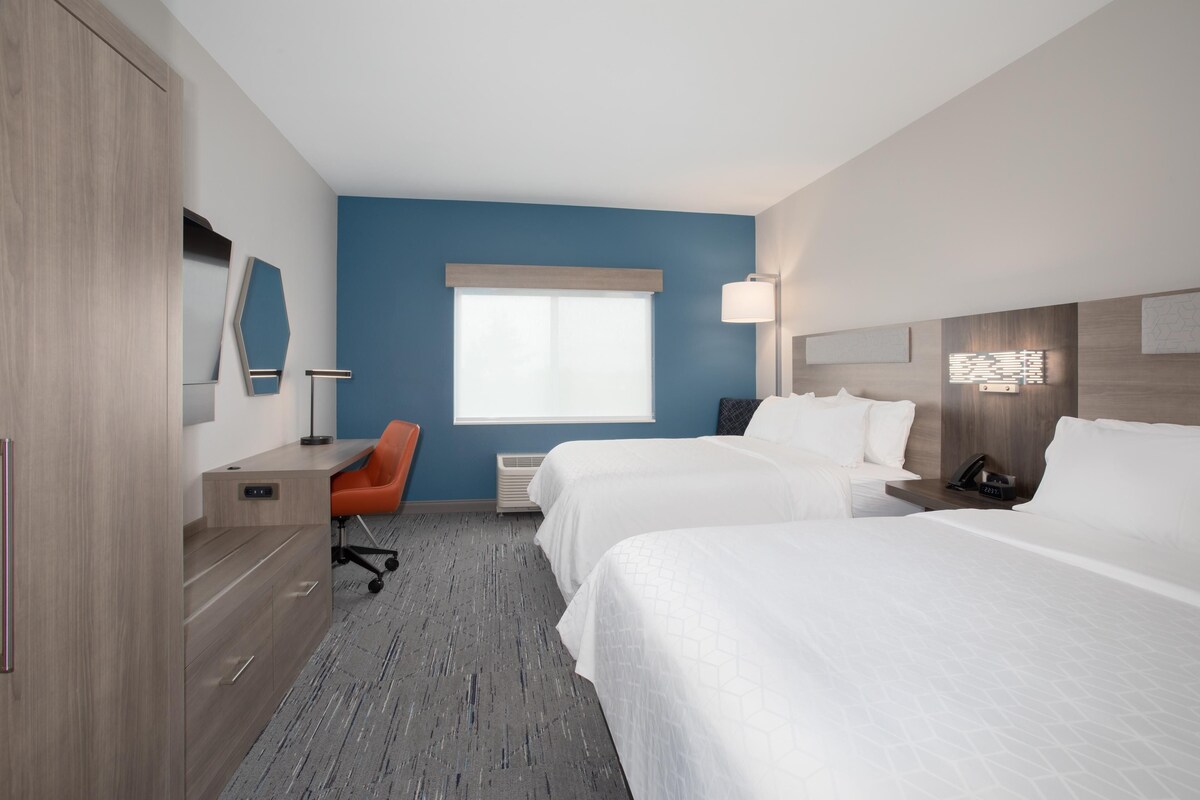 Une chambre d’hôtel avec deux lits, un bureau, une chaise, une lampe et une fenêtre.