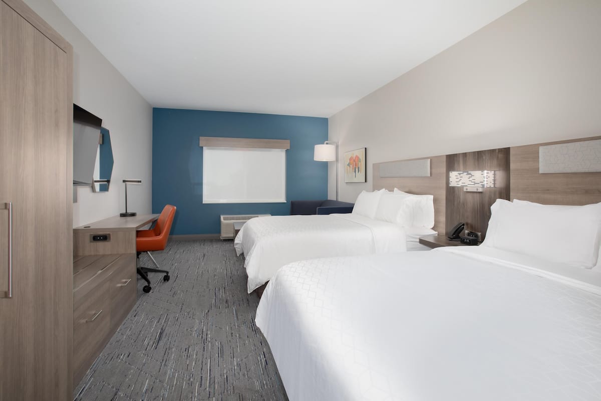 A hotel room with two beds, a desk, a chair, a desk lamp, a telephone, and a window with blinds.