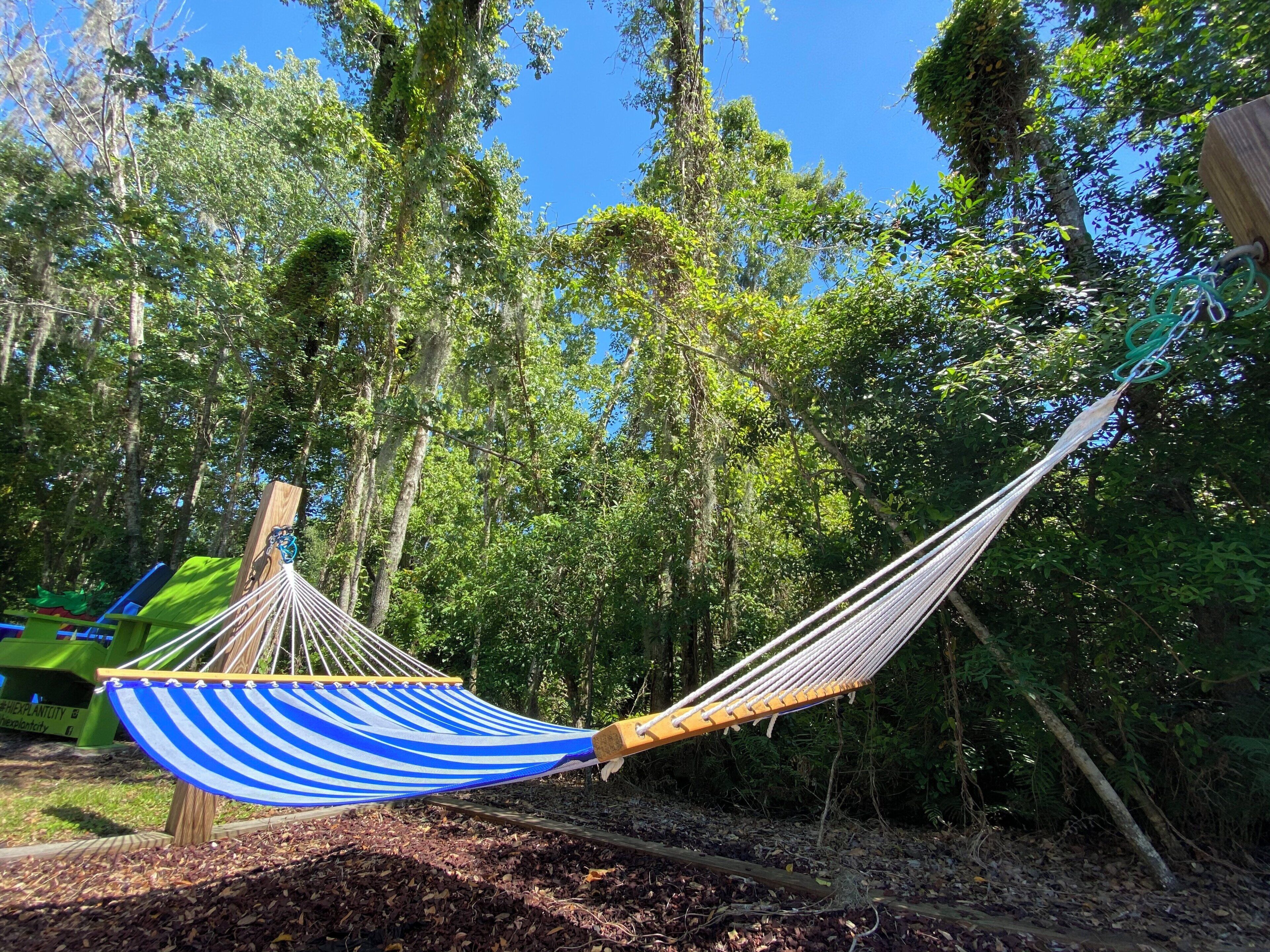 A hammock suspended between wooden posts in a wooded area with a clear sky.