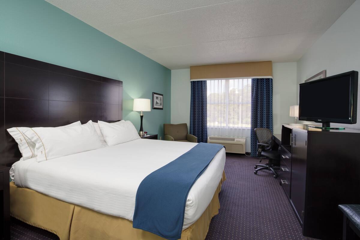 Une chambre d’hôtel avec un grand lit, un bureau avec un ordinateur, une télévision et une chaise.