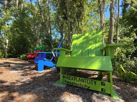 Una silla verde con un símbolo de hashtag y nombres de usuario de redes sociales, rodeada de árboles y un área boscosa.