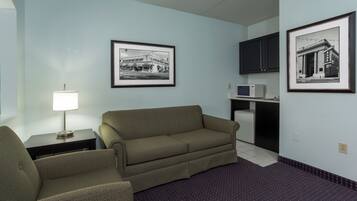 Habitación de hotel con sofá, sillón, cuadros en la pared, microondas y un mueble pequeño.