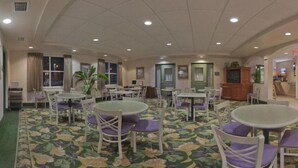 Een restaurant in een hotel, met meerdere ronde tafels en stoelen, een kamerbreed tapijt en een plafond met inbouwspots.
