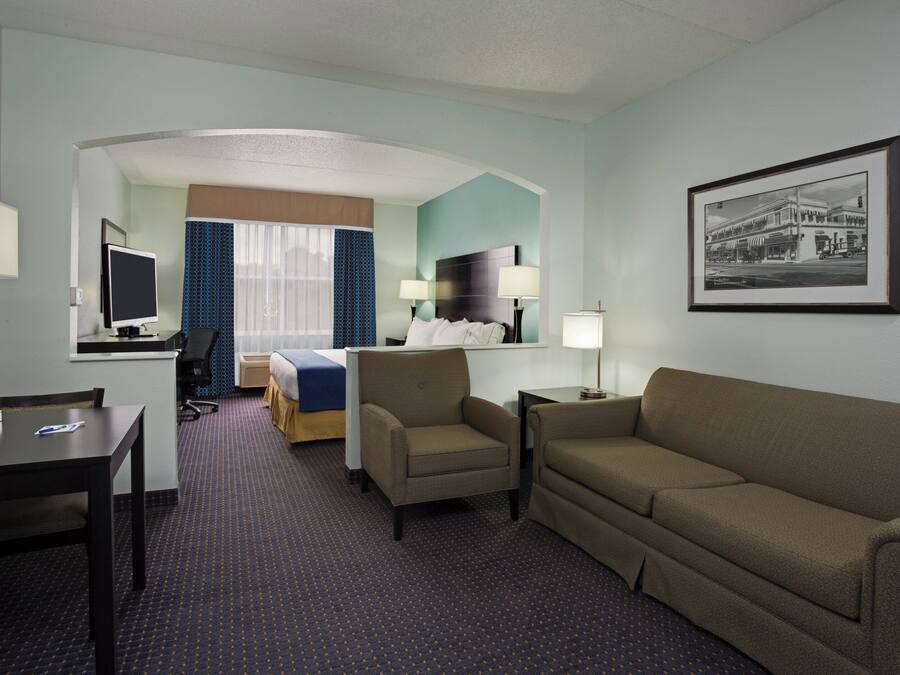 A hotel room with a bed, a desk, a chair, a sofa, and a television.