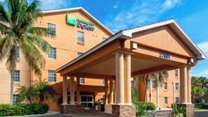 A Holiday Inn Express building with a covered entrance, palm trees, and a clear sky. - Holiday Inn Express & Suites Naples North - Bonita Springs by IHG (Bonita Springs)