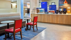 A hotel lobby with seating, a bakery counter, and coffee machines.