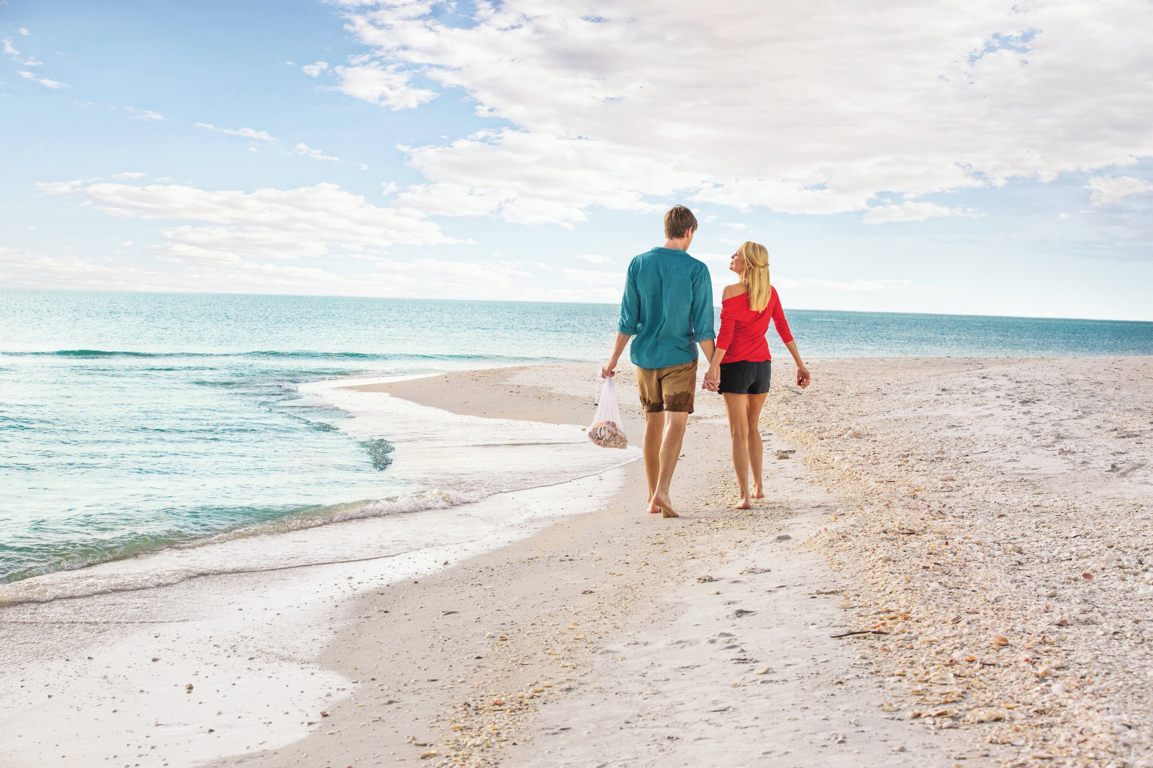 Una pareja caminando sobre una playa arenosa con el océano al fondo.