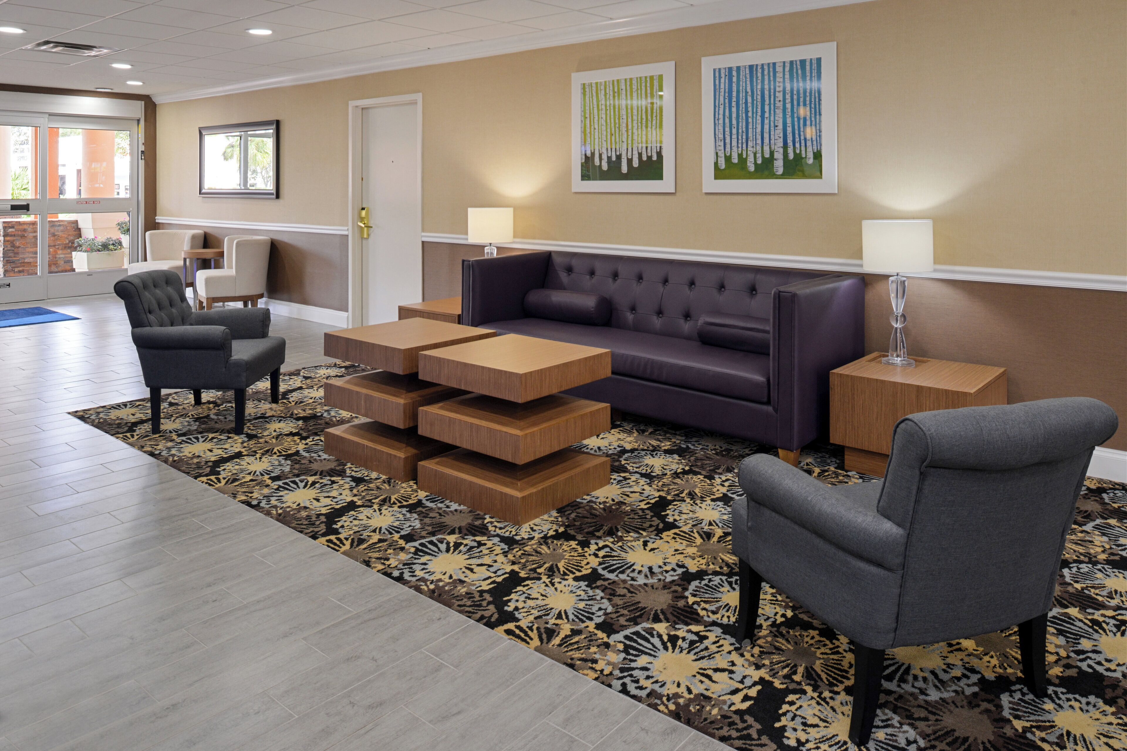 A hotel lobby with a sofa, armchairs, a coffee table, and a patterned rug.