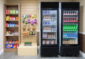 Ein Getränkeautomat mit Snacks und Getränken, ein Regal mit verpackten Waren und eine Vitrine mit Kleinartikeln an der Wand.
