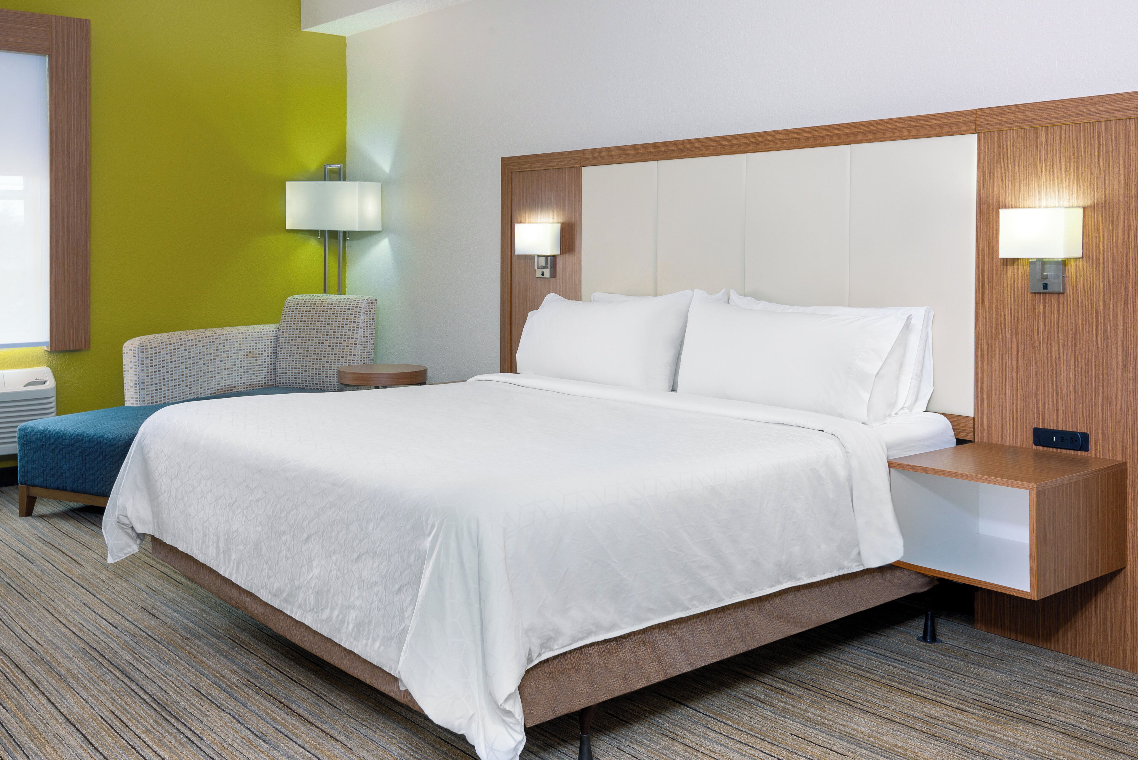 A hotel room with a large bed, bedside tables, a lamp, and a chair.