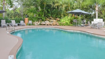 A swimming pool with lounge chairs and umbrellas, surrounded by lush greenery.
