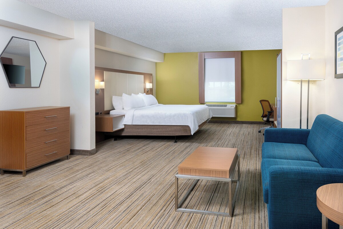 Ein Hotelzimmer mit Bett, Schreibtisch, Stuhl, Kommode und Lampe.