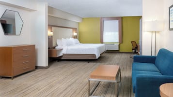 A hotel room with a bed, a desk, a chair, a dresser, and a lamp.