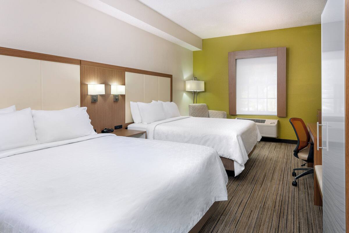 Ein Hotelzimmer mit zwei Betten, einem Schreibtisch, einem Stuhl, einer Lampe und einem Fenster.